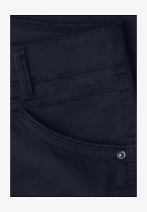 Tumma laivastonsininen farkut lähikuvassa, jossa näkyy etutasku, vyölenkki ja metallinen niittiyksityiskohta.