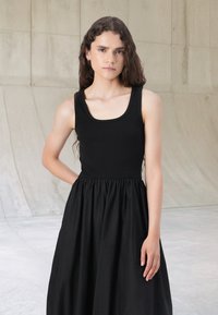 Black dress with a ribbed bodice and a gathered, flowing skirt. The neckline is wide, and fabric appears smooth with a matte finish.