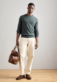 Grøn strikket trøje, crème farvede bukser, brun læder duffeltaske og brune støvler. Glat strik tekstur, simpelt design og neutral farvepalette.