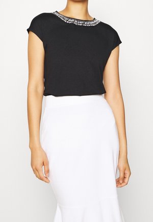 Musta paita lyhyillä hihoilla, jossa on koristeellinen helmi- ja timanttinelikko. Sileä kangas, rento istuvuus, yhdistetty valkoiseen hameeseen.