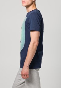 Navy modrá bavlněná T-shirt s krátkými rukávy a grafickým potiskem na přední straně. Standardní střih s kulatým výstřihem.