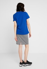 Modrá bavlněná trička spárovaná s černobílou sukní s kostkovaným vzorem a rozparkem vzadu. Nosit s černými teniskami.