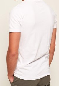 T-shirt blanc à manches courtes avec col rond et texture en coton lisse, vu de dos, porté avec un pantalon vert olive.