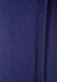 Tissu tricoté bleu foncé avec des coutures visibles et une texture en gros plan, montrant une couture verticale sur le côté droit.