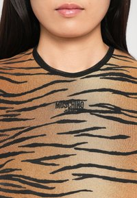 Femeie îmbrăcată cu o cămașă cu dungi de tigru, cu tiv negru și logo-ul "Moschino Jeans" brodat pe piept.