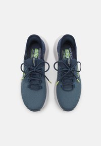 Zapatillas deportivas de malla azul marino con punta redondeada, suela flexible y detalles en verde lima contrastante en los cordones y la marca.