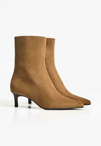 Paire de bottines en daim marron avec bouts pointus et petits talons kitten sur fond blanc.
