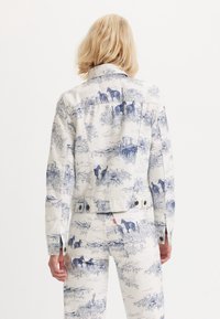 Bílá džínová bunda s modrým potiskem koně a krajiny, s klasickým límečkem, dlouhými rukávy a knoflíkovými detaily na zádech.