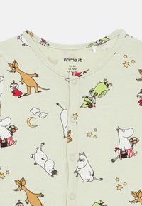 Lys grønn bodysuit med et tegneserie-mønster som viser ulike fantasifulle figurer, skyer og stjerner. Trykknapplukking foran.