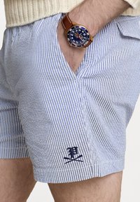 Siniset ja valkoiset raidalliset shortsit, joissa on sinisellä ommeltu logo. Puuvillamateriaali, rento malli, jossa on sivutaskut ja litteä vyötärö.