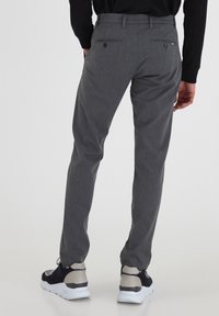 Pantalones grises a medida hechos de tela texturizada. Incluyen dos bolsillos traseros con botones, trabillas para cinturón y un diseño de corte slim.