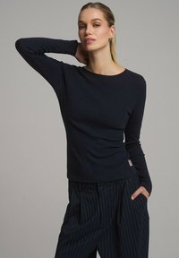 Granatowy top z długim rękawem wykonany z prążkowanej tkaniny, z okrągłym dekoltem, dopasowaną sylwetką i minimalistycznym wzornictwem. W zestawie ze spodniami w paski.