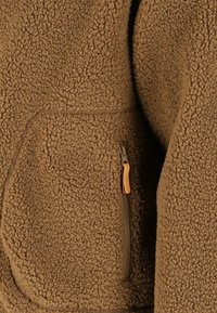 Brun tekstureret fleecejakke lomme med lodret lynlås og lysebrun læderlynlåsåbnertab.