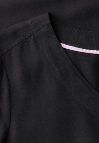 Tessuto nero con design a V, caratterizzato da una superficie liscia e un accento contrastante di rosa chiaro lungo il collo.