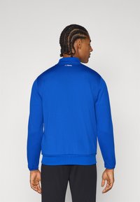 Royal blue treningsjakke med teksturert finish, høy krage, ribbestrikkede mansjetter og nederkant, samt "FC Porto"-logo på baksiden av nakkesømmene.