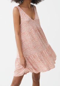 Robe florale en tissu doux avec un décolleté en v, sans manches et une silhouette évasée arborant un motif léger orange et blanc.