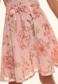 Rochie florală roz cu textură strălucitoare, având un corset ajustat și o fustă evazată. Include o curea cu fundă și un overlay de modele florale delicate.