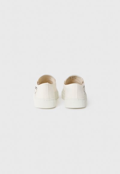White canvas sneakers with a low-back design, rubber soles, and subtle stitching detail on the heel. Minimalist style with no visible logos.