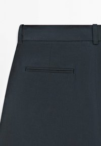 Gros plan sur un pantalon gris foncé cintré montrant la ceinture avec passants pour ceinture et une poche passepoilée simple à l'arrière.