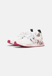 White athletic sneakers with colorful floral accents, textured mesh upper, pink rubber sole, and gold logo on the side.