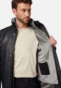 Schwarze Lederjacke mit grauem Fellfutter, ausgestattet mit einem Reißverschluss und zwei Knöpfen auf der Vorderseite; beinhaltet eine kleine Innentasche.
