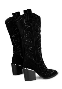 Botas de vaquera de ante negro con costuras decorativas y acentos de tachuelas. La diseño se completa con punteras cuadradas y tacones gruesos.