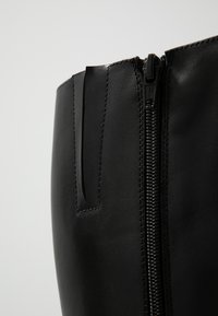 Bottine en cuir noir avec fermeture éclair sur le côté, au design épuré et avec des détails de couture. Le matériau a une texture lisse et semble durable.