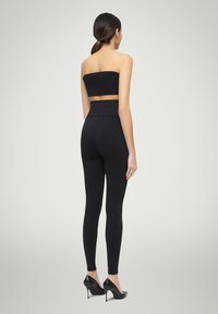 Top nero senza spalline abbinato a leggings neri a vita alta con texture a coste, completando l'outfit con décolleté nere con tacco a stiletto.