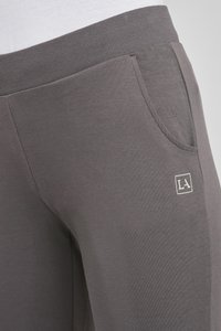 Graue Jogginghosen mit einem gerippten Bund, seitlicher Tasche und einem weißen quadratischen Logo am unteren linken Bein. Weicher Stoff und lässige Passform.