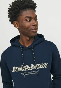 Sudadera con capucha azul marino con el logo blanco y dorado "Jack & Jones." Presenta cordones ajustables con un patrón en blanco y negro contrastante.