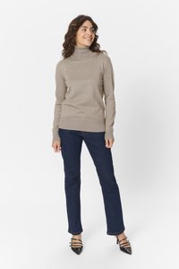 Beiger Rollkragenpullover, feine Strickqualität, körperbetontes Design. Kombiniert mit dunkelblauen Jeans, leicht ausgestelltem Schnitt am Knöchel und schwarzen spitzen Pumps.