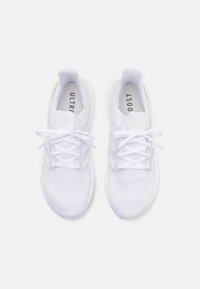 Zapatos deportivos blancos con parte superior de malla, cuello acolchado, logo de tres rayas y cordones planos, con una suela redondeada para mayor amortiguación.