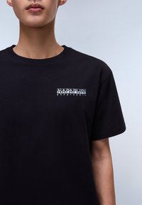 Black cotton t-shirt featuring a white graphic logo on the left chest area. Short sleeves and a crew neck design. Smooth texture.