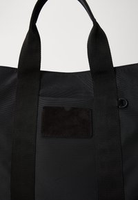 Czarna torba tote z nylonu z mocnymi tkaninowymi uchwytami, z teksturowaną czarną zamszową łatą do przechowywania kart oraz trwałym, bezszwem wzornictwem.