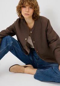 Giacca in pile marrone con un motivo geometrico, bottoni a scatto, abbinata a jeans in denim azzurro chiaro e scarpe slip-on in suede beige.
