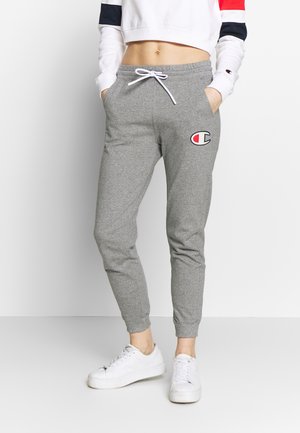 Pantalon de survêtement gris avec un design fuselé, taille à cordon de serrage et poches latérales. Présente un logo brodé sur la hanche gauche.