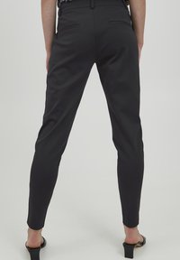 Mustad, istuvad püksid siledast tekstuurist. Omavad kitsast jala disaini ja kahte tagumist taskut. Kangas tundub elastne ja läikiv.