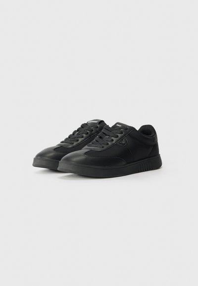 Black sneakers featuring a smooth leather upper, lace closure, padded collar, and a textured rubber sole with subtle branding on the tongue.