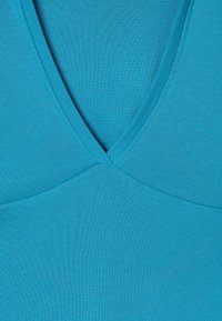 Blue fabric with a deep V-neckline and visible stitching along the edges, showing close-up detail of a garment's front section.