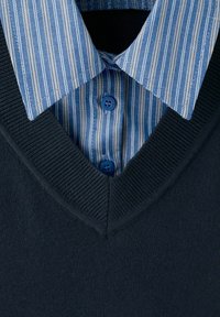 Blå- og hvidstribet skjortekrave under en mørkeblå V-hals strikket sweater.