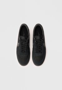 Melni Nike sporta apavi ar zamšas un režģa augšdaļu, apaļu purngalu, auklu aizdari un gumijas zoli, ar diskrētu logotipu sānos.