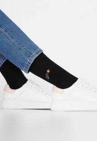 Czarne skarpetki z prążkowanym wzorem, zdobione haftowaną pomarańczową gwiazdą i kolorowymi paskami, w połączeniu z białymi sneakersami i niebieskimi dżinsami.