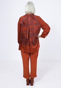 Luftige, dunkelrote Bluse mit einem transparenten floralen Rücken, gepunktet, kombiniert mit passenden roten Hosen und braunen Blockabsatzschuhen.