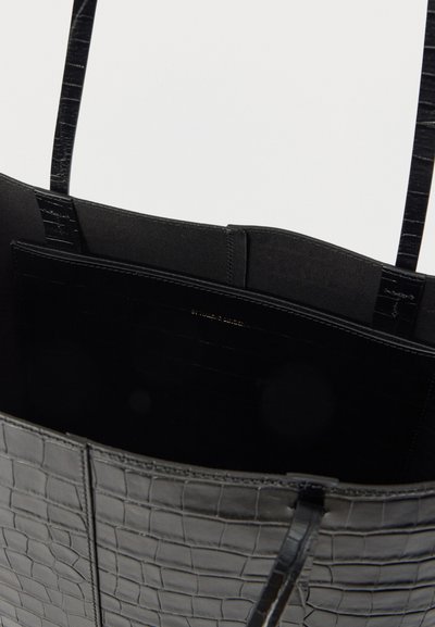 Μαύρη τσάντα tote με ανάγλυφη υφή κροκοδείλου, που δείχνει εσωτερική τσέπη και δύο λεπτούς ιμάντες ώμου.