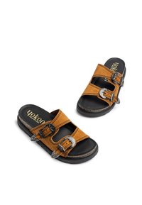 Sandales en daim marron avec deux brides réglables ornées de boucles de couleur argentée, un semelle intérieure rembourrée noire et une semelle texturée.