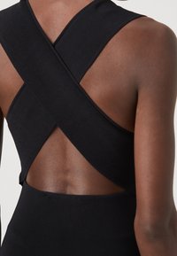 Body noir côtelé avec un design croisé dans le dos. Le tissu semble texturé, mettant en valeur une silhouette ajustée avec une finition lisse.