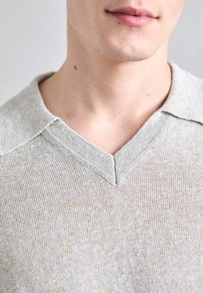 Pull en V de couleur beige clair avec de légers éclats bleus, présentant un tricot texturé et un col plat.