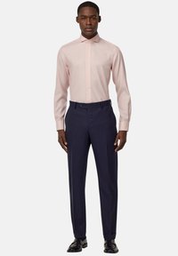 Camicia rosa chiaro con colletto a punta e apertura con bottoni, abbinata a pantaloni neri su misura e scarpe nere.