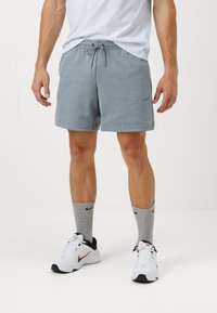 Pantaloni scurți gri, fabricați dintr-un amestec moale de bumbac, cu un talie elastică și șnur de ajustare. Asortați cu adidași albi și șosete gri.
