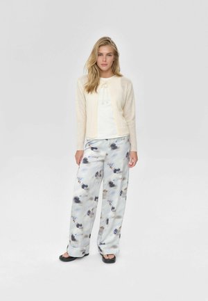 Vaaleanbeige neuletakki teksturoiduilla hihoilla, valkoinen paita solkityylillä ja kuviolliset leveälahkeiset housut pehmeissä sinisen, harmaan ja mustan sävyissä.